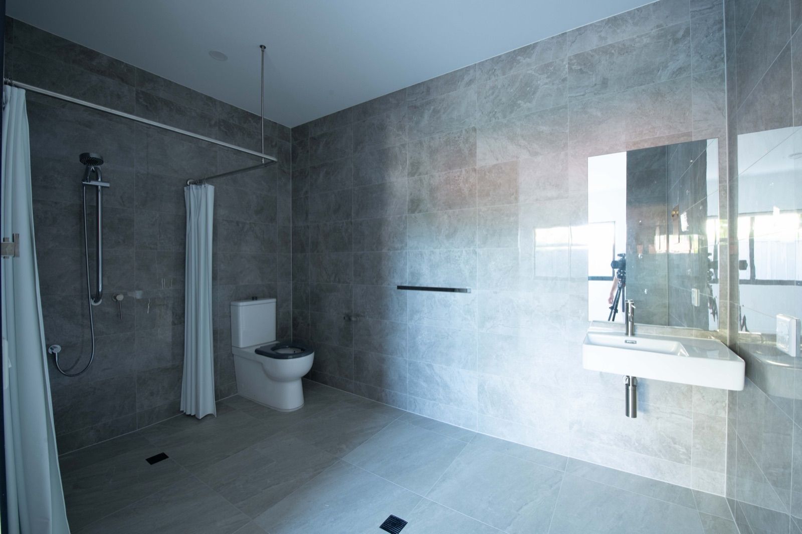 Photo 6 of 11: Accessible bathroom with a step-free shower area, handheld shower, wall-mounted basin and grab rail