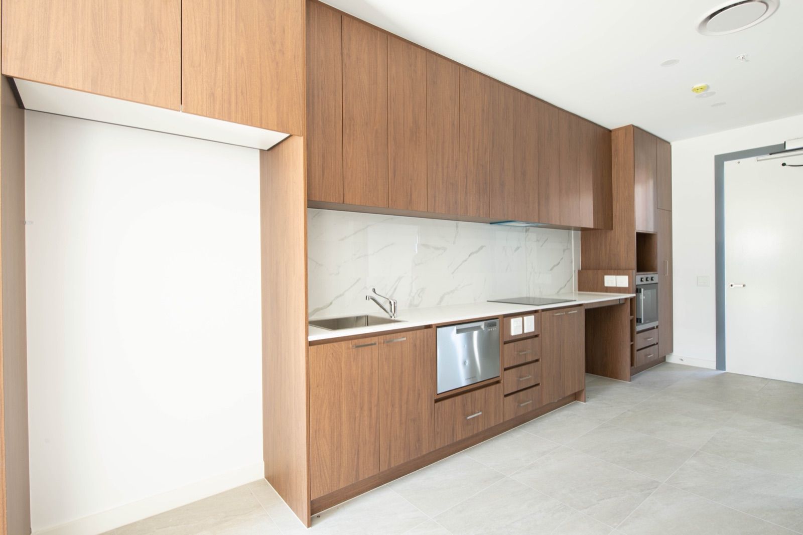 Photo 3 of 11: Full-length villa kitchen with timber cabinets, stone benchtop, wall oven and open space beneath the bench
