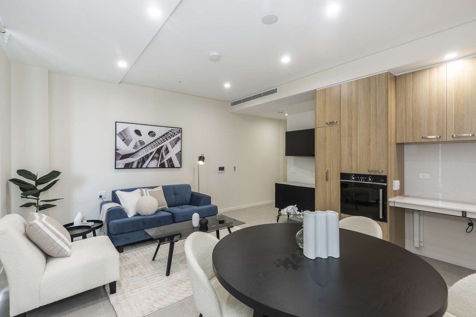 Photo 2 of 11: Open-plan living and dining area with a blue sofa, round dining table and kitchen behind