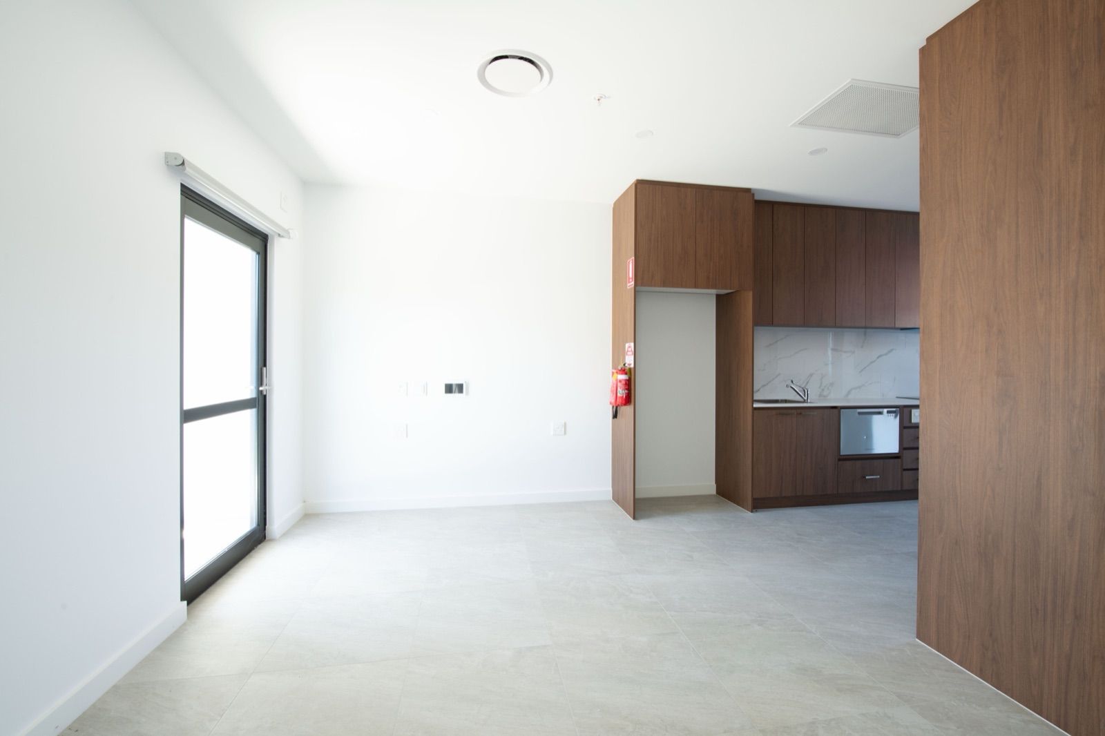 Photo 2 of 11: Open living area with a wide glass door, tiled floor and the kitchen beyond